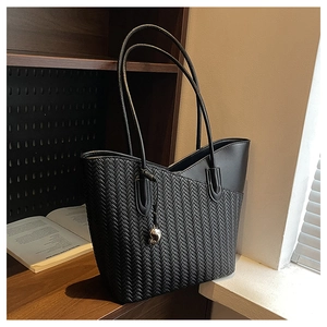 Close-up of black woven tote bag with smooth leather trim and silver heart charm detail
