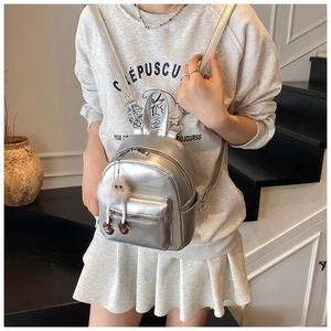 Close-up of metallic silver mini backpack with plush pendant and metal zippers