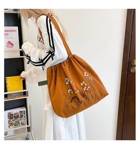 Detailed embroidery of colorful flowers on a large orange canvas drawstring tote bag