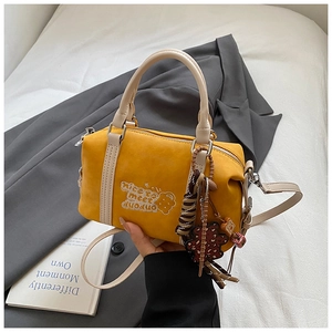 Detail der gelben Boston-Tasche mit Stickerei und süßen Anhängern auf weißem Betttuch