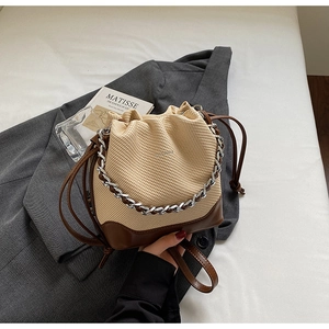 Detail of drawstring bucket bag with beige woven texture and brown leather base