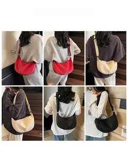Detail view of crescent crossbody bags in red, beige, and black with V-shaped stitching