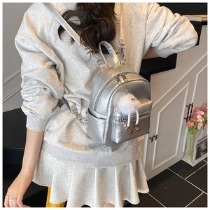 Close-up of a mini silver metallic backpack with a white fuzzy charm on a model's back
