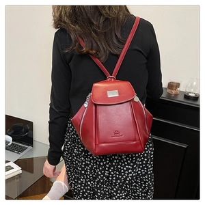 Red leather backpack shown from behind on model in a cozy home office setting