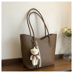 Detail der braunen Leder-Tote-Bag mit Litschi-Muster und niedlichem Plüschbär-Anhänger