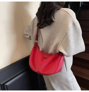 Close-up of red crescent shoulder bag worn by model against a minimalist studio wall
