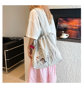 Detail of floral embroidery on light gray canvas tote bag with drawstring closure