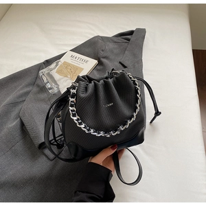 Detail of a black woven drawstring bucket bag with silver chain handle on white linen