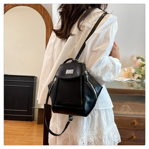 Detail of a black leather backpack with silver metal plate and side zipper on a model