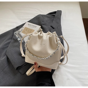 Detail of cream bucket bag with fabric texture, silver chain, and drawstring closure