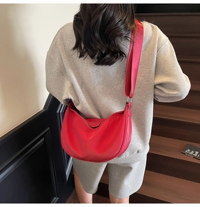 Close-up of a red nylon half-moon crossbody bag featuring a wide strap on a model