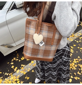 Détail du sac seau en laine à carreaux avec poignées en cuir marron et breloque en cœur