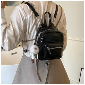 Close-up of shiny black mini backpack with silver zippers and white plush keychain accessory