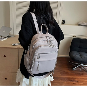Detail of light grey pebbled leather backpack featuring silver ring zippers and woven straps