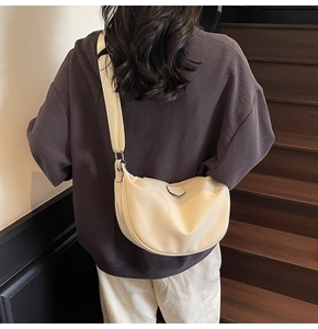 Detailed close-up of beige moon-shaped shoulder bag with wide fabric strap and metal logo