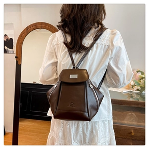 Detailed back view of a dark brown vintage backpack worn by a model in a cozy room