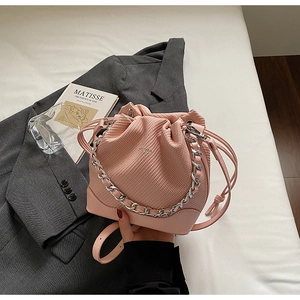Detail of pink quilted bucket bag with silver chain strap and drawstring on grey suit