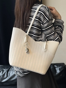 Chic cream woven tote bag with leather trim and metal charm shown on model's shoulder