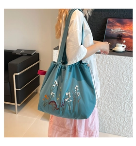 Detail of floral embroidery on a teal drawstring tote bag with pink side ribbon