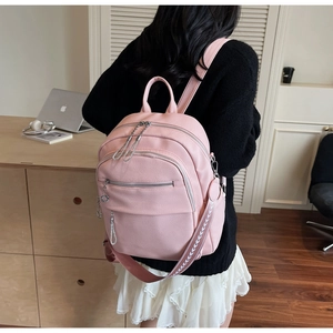 Pink faux leather backpack with multiple zippers and decorative chain detail on female model