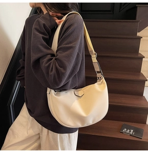 Chic cream half-moon hobo bag detail worn by model on stairs with adjustable wide strap