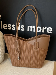 Retro brown woven leather tote bag with long straps and heart charm on beige surface