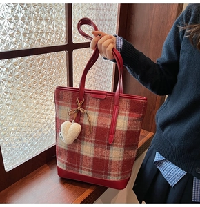 Détail du sac cabas en laine à carreaux avec bordure en cuir rouge et breloque cœur