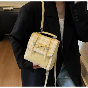 Close-up of a yellow plaid handbag with a bow detail worn by a model in a black suit