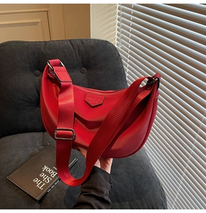 Detail of red crescent shoulder bag with metallic logo plaque and adjustable strap