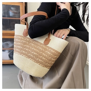 Close-up of a woven straw tote bag featuring brown leather straps and intricate braid details