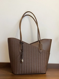 Brown leather woven tote bag with slim shoulder straps and metallic charm pendant