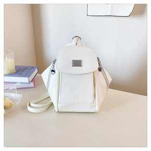 Detail of cream white PU leather backpack with geometric flap and metal clasp on desk