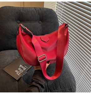 Close-up of red nylon half-moon bag with adjustable shoulder strap and logo detail