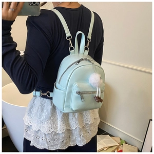 Close-up of mint blue mini backpack with plush pompom and doll charm on a female model