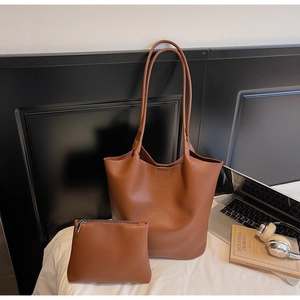 Detailed view of brown lychee grain leather tote bag set on bed showing matte texture