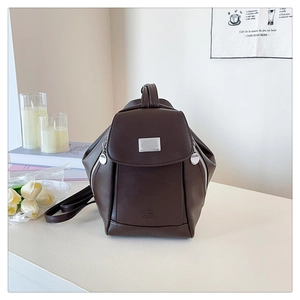 Detail of deep brown leather backpack featuring a silver metal plate and side zippers