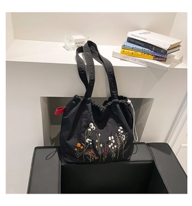 Detail of floral embroidery on a black nylon tote bag with drawstring closure and strap