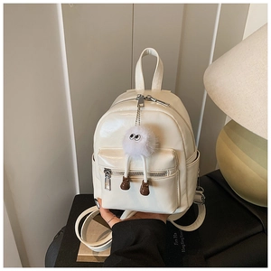 Detail of glossy cream mini backpack featuring a plush eye charm and silver metal zippers