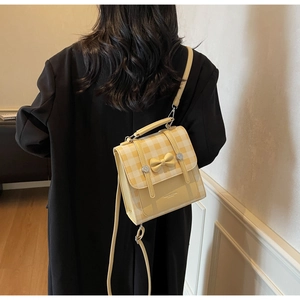 Detail of yellow checkered bow handbag styled with a black coat for commuter look