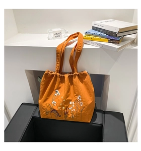 Detail of orange canvas tote with floral embroidery and drawstring closure system