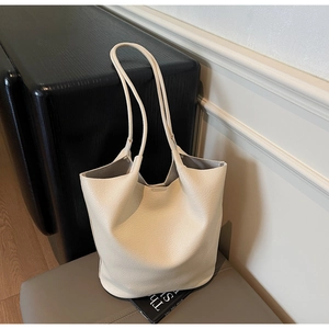 Detail of minimalist off-white lychee pattern leather tote bag on a grey textured stool