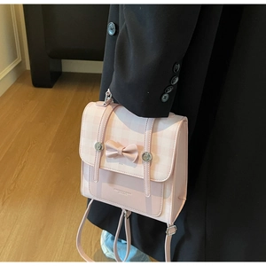 Detail of pink bow mini backpack with checkered flap and leather texture displayed indoors
