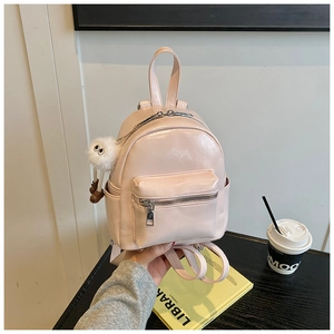 Detail of a mini light pink high-gloss PU backpack with a white plush monster keychain charm
