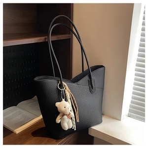 Detailansicht der schwarzen Tote Bag aus Leder mit Bärenanhänger auf Holzregal