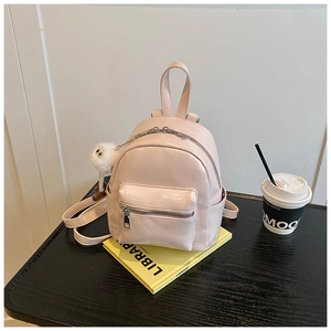 Close-up of a mini pink PU leather backpack with a plush ball charm on a wooden table