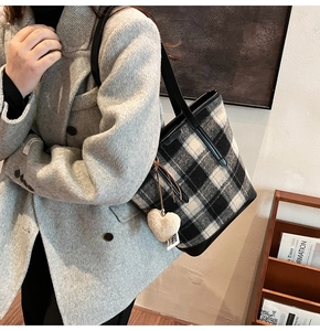 Detail of checkered wool tote bag with heart charm and black leather strap in modern interior