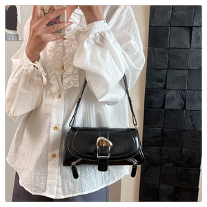 Detail of a black soft leather shoulder bag with a large silver buckle and metal zippers