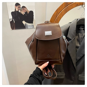 Detail of dark brown leather backpack showing logo embossing and silver zipper accents