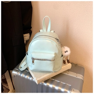 Mint green mini leather backpack with plush monster pendant on a silver suitcase