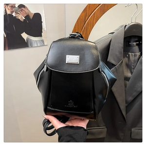 Detail view of glossy black leather backpack with rectangle metal plate and side zippers